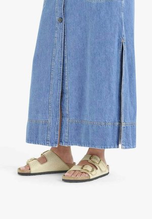 Gonna di denim con spacchi laterali e bottoni, abbinata a sandali bassi beige chiaro con cinturini testurizzati e due fibbie regolabili.