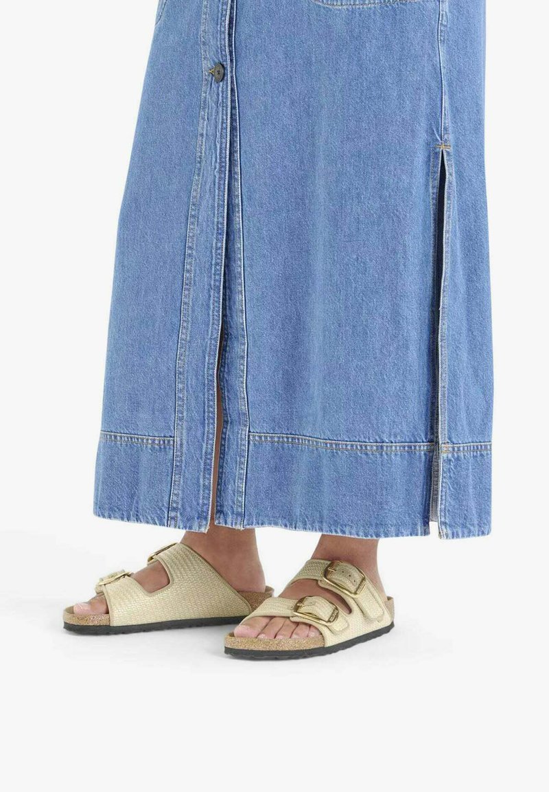 Gonna di denim con spacchi laterali e bottoni, abbinata a sandali bassi beige chiaro con cinturini testurizzati e due fibbie regolabili.