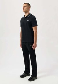 Svart polo t-shirt med vita ränder på kragen, kombinerad med svarta byxor med en guldtipp. Slät tyg, minimalistisk design.