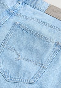 Jeans de denim azul claro que presentan un bolsillo trasero con costuras en contraste y una etiqueta de parche de cuero en la cintura.