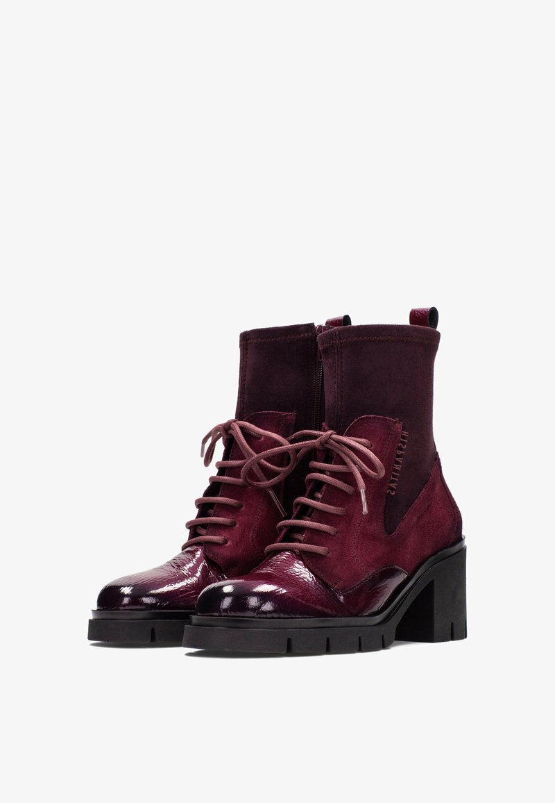 Un par de botines oscuros burdeos con tacones gruesos, parte delantera con cordones, texturas de ante y cuero brillante, y cremalleras laterales.