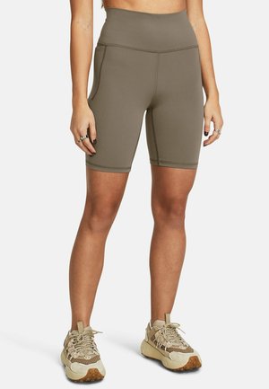 Frau trägt hoch taillierte olivgrüne Radlerhose und beige Sportsneaker, steht mit entspannten Armen an den Seiten.