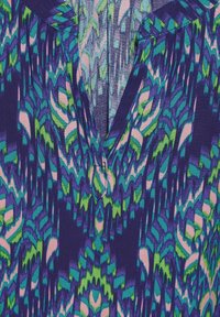 Gros plan d’un tissu avec un motif abstrait en forme de plume en vert, bleu, rose et violet sur un fond sombre.