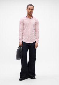 Hellrosa Button-up-Hemd, dunkle Schlagjeans, schwarze Lederschuhe und eine schwarze Tasche. Minimalistisches Design, glatte Texturen und taillierte Passform.