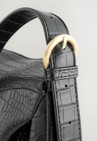 Sac à main en cuir noir avec un motif crocodile texturé, un accent en métal doré et une bandoulière ajustable avec une finition lisse.