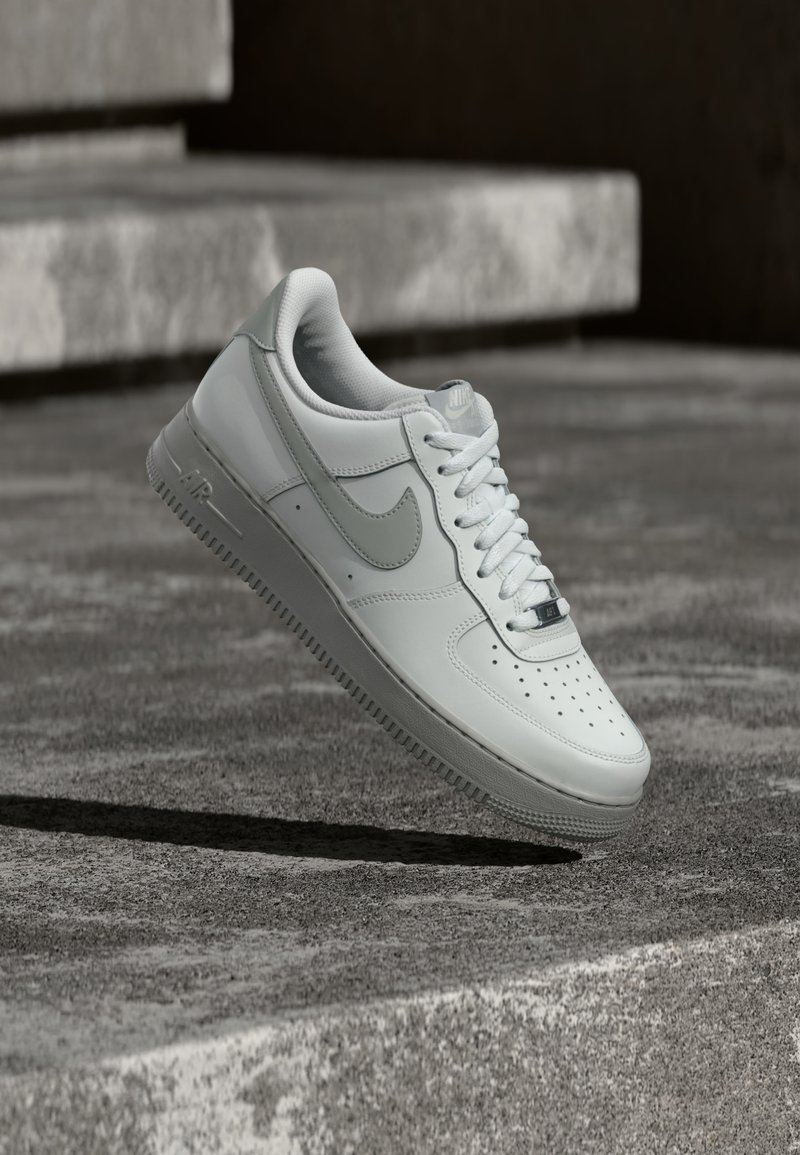 Scarpa da ginnastica Nike Air Force 1 bianca che fluttua sopra una superficie di cemento strutturato con scalini di pietra sullo sfondo.