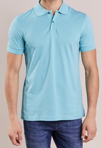 Polo light bleu en tissu lisse, doté d'un col rabattu, de deux boutons et d'un logo discret sur la poitrine. Manches courtes.