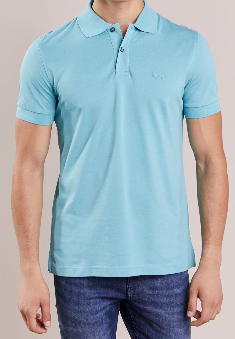 Polo light bleu en tissu lisse, doté d'un col rabattu, de deux boutons et d'un logo discret sur la poitrine. Manches courtes.