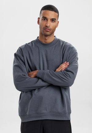 Gray sweatshirt with a round neckline, ribbed cuffs, and hem. Features a smooth texture and a small logo detail on the chest.