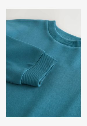 Sudadera en color azul verdoso con cuello redondo y puños acanalados. Textura suave, con un corte relajado y sin patrones ni detalles de herrajes visibles.