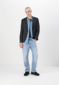 Blazer iz temnosive tkanine nad svetlo modro denim srajco, v kombinaciji s svetlo modrimi kavbojkami in črnimi supergami. Preprost, sproščen kroj.