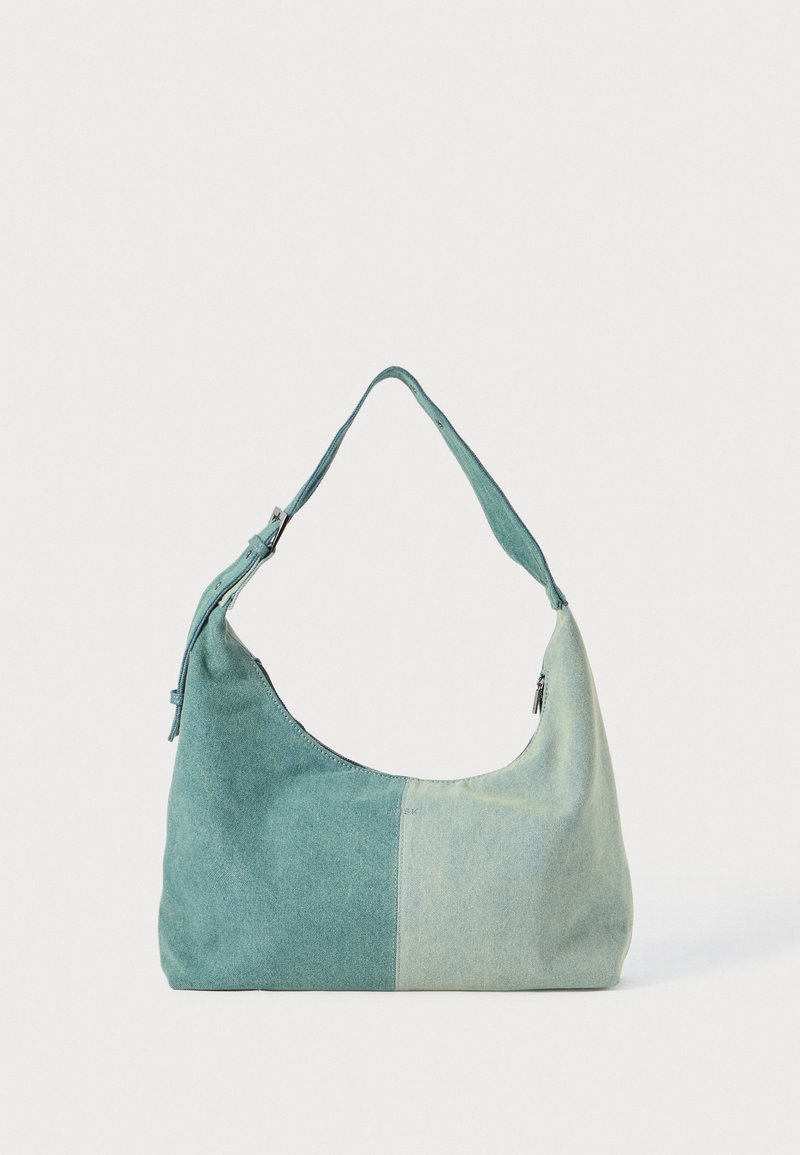 Borsa a spalla in canvas di colore verde chiaro e teal, con forma curva, chiusura a zip e una singola tracolla regolabile. Texture liscia, senza dettagli hardware visibili.