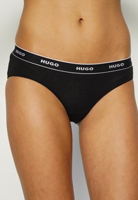 Culotte de bikini en coton noir avec une large ceinture arborant le logo blanc "HUGO". Texture lisse et design classique et minimaliste.