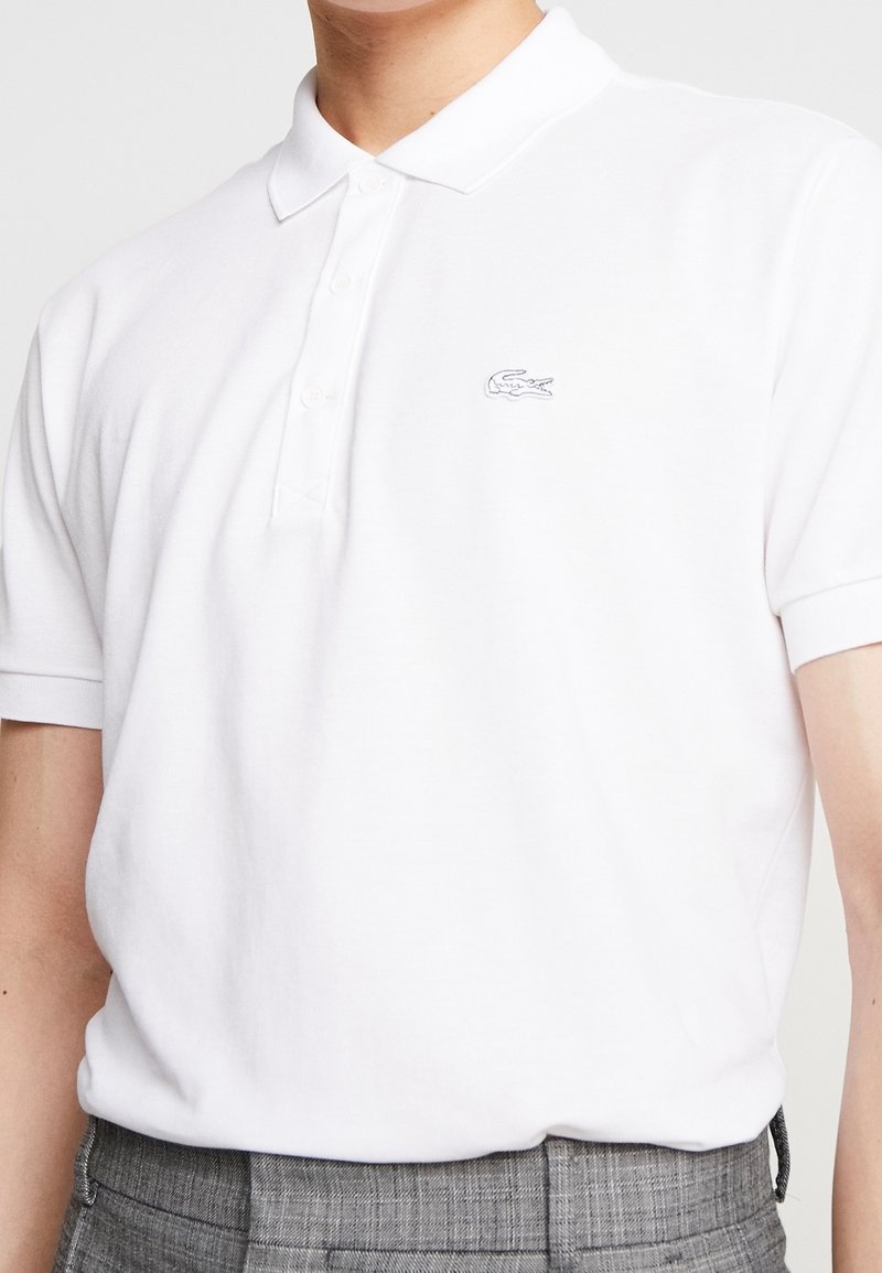 Polo blanc en coton, doté d'une patte à trois boutons et d'un petit logo brodé sur le côté gauche de la poitrine. Manches courtes.
