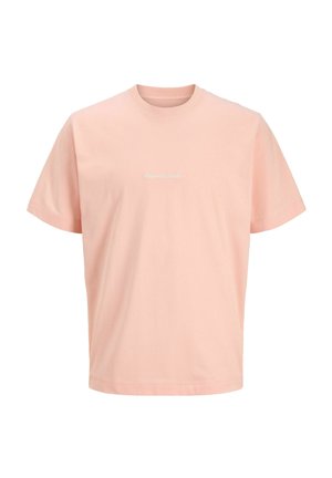 Adolescent garçon debout regardant à droite, portant un T-shirt rose clair, un short noir avec texte blanc, des chaussettes crème et des baskets blanches avec des rayures noires.