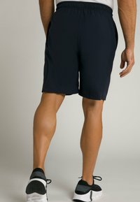 Pantalones cortos deportivos de un azul marino oscuro con cintura elástica, que cuentan con bolsillos laterales y una tela suave y ligera, combinados con zapatillas negras.