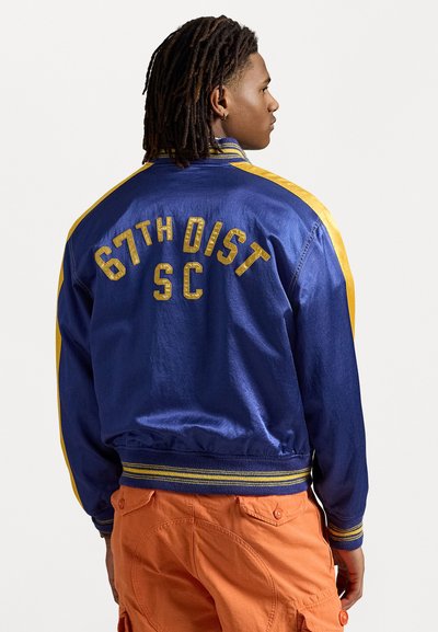 Marineblaue Jacke mit gelben Akzenten, auf der Rückseite mit "67TH DIST SC" in fetter Schrift. Gerippte Bündchen und Saum, glatte Textur.