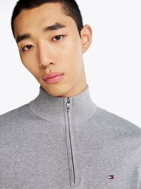 Grauer Reißverschluss-Pullover mit geripptem Kragen, der ein kleines Logo auf der Brust trägt. Weicher Stoff und minimalistisches Design.