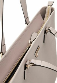 Sac fourre-tout texturé rose clair avec fermetures zippées dorées, accents noirs et un détail en métal géométrique. Il dispose de poignées doubles pour le porter.