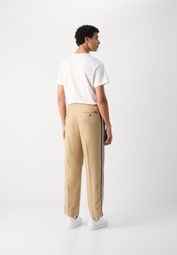 Beige bukser med sidelister og elastisk talje, kombinert med en enkel hvit T-skjorte. Glatt stoff, avslappet passform, to baklommer.
