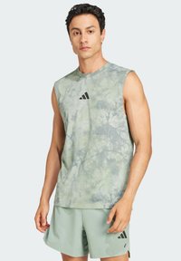 Bezrękawnik sportowy w jasnym zielonym kolorze z teksturowanym wzorem tie-dye; posiada czarne logo Adidas na klatce piersiowej oraz pasujące szorty.