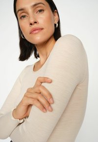 Hellbeiger, gerippter Langarm-Top mit Rundhalsausschnitt, das dezent geraffte Stoffe an den Manschetten und eine glatte Textur aufweist.