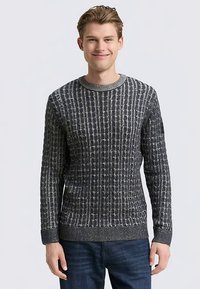 Grauer Strickpullover mit einer strukturierten, gemusterten Gestaltung und geripptem Halsausschnitt sowie Bündchen. Kombiniert mit dunkelblauen Jeans.