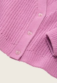 Roze gebreide cardigan met een gestructureerd patroon, voorzien van hartvormige knopen en ribbels aan de mouwen. Zacht, comfortabel materiaal, met een open voorkant.