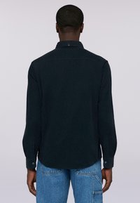 Camicia a maniche lunghe di un blu navy scuro con colletto a punta, polsini abbottonati e orlo arrotondato. Il tessuto sembra liscio e di peso medio.