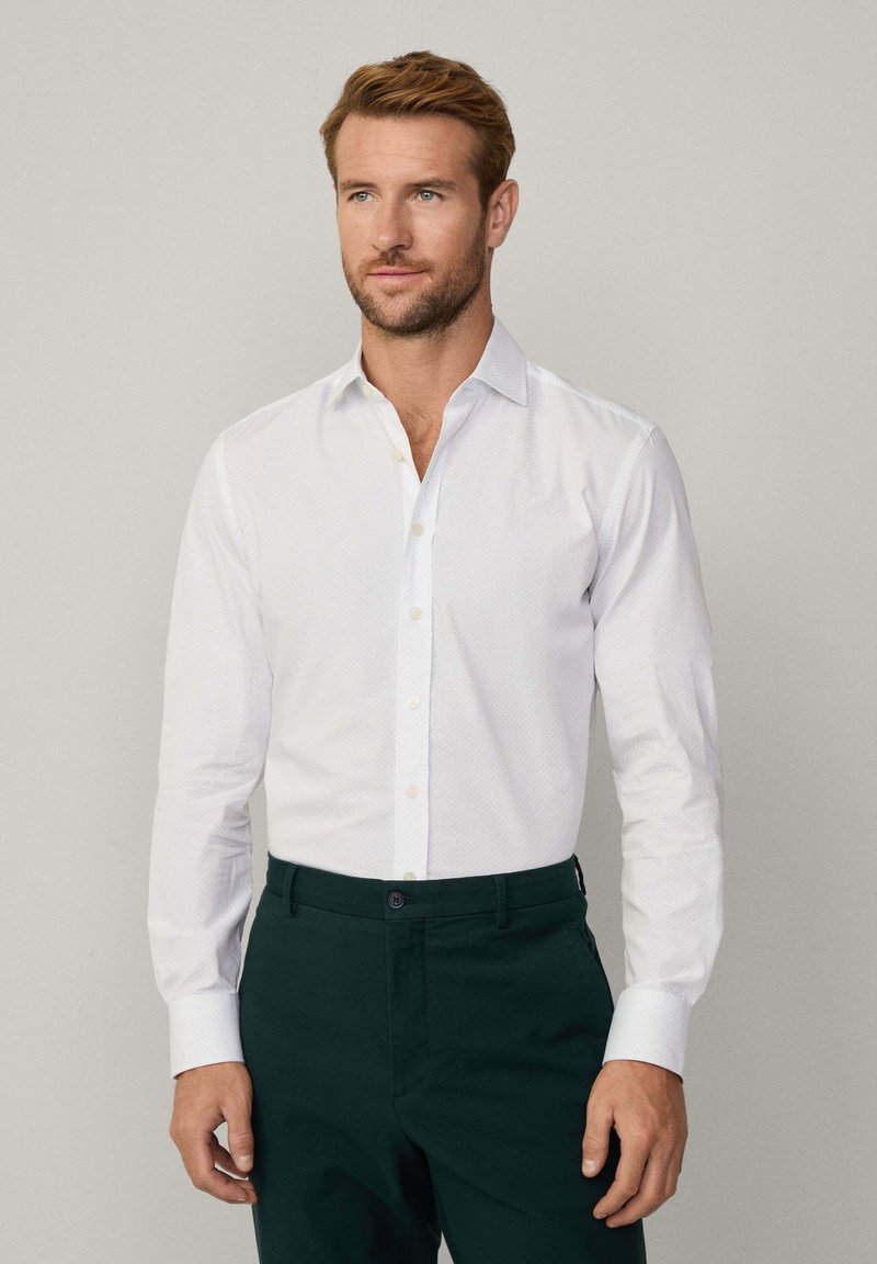 Camicia bianca con un motivo sottile, maniche lunghe e chiusura con bottoni, abbinata a pantaloni verde scuro. Tessuto liscio, vestibilità su misura.