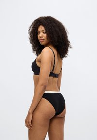 Σετ μαύρου εσωρούχου με ένα λείο, χωρίς ενίσχυση σουτιέν με ρυθμιζόμενες τιράντες και ένα ταίριαστο σλιπ χαμηλής μέσης με αντίθετη μέση.