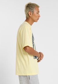 T-shirt en coton jaune à manches courtes, avec un design graphique en bleu foncé sur le devant. Coupe simple et décontractée.