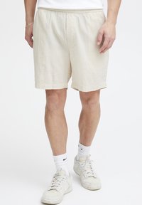 Beige shorts med strukturmønster, elastisk midjebånd og sidelommer, brukt med hvite sneakers og ankellange sokker.