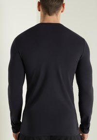 Langärmeliges schwarzes Shirt aus glattem Stoff, mit figurbetonter Passform, Rundhals und verstärkten Nähten an den Manschetten und dem Saum.