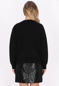 Pulover negru din lână cu o croială lejeră, având un tiv côtat și îmb embellismente pe umeri. Asortat cu o fustă texturată neagră lucioasă.