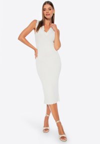Witte midi-jurk met een geschulpte halslijn en zoom, getailleerde vorm, geribbelde textuur, gecombineerd met nude haksandalen met bandjes.