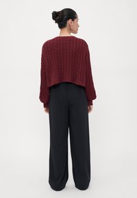Maroon cable-knit cropped sweater with a loose fit and long sleeves paired with black wide-leg trousers. Simple, textured design.
