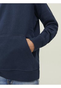 Sweat-shirt bleu marine en tissu doux, doté d'une poche à l'avant et de poignets côtelés. Coutures apparentes soulignant l'ourlet et la poche.