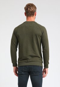 Felpa verde oliva con un motivo geometrico testurizzato, polsini e orlo a costine. Presenta un collo a giro e maniche raglan.