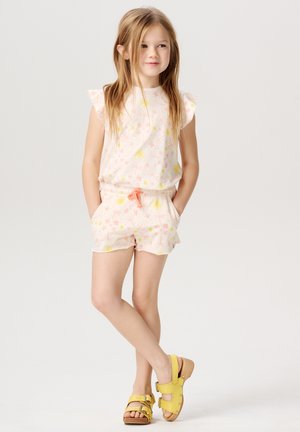 Ensemble à imprimé floral rose clair avec des manches volantées, un short à taille élastiquée et un cordon orange. Associé à des sandales jaunes.