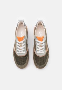 Atletiska sneakers med ett mesh-överdel i olivgrön, beige och grå. Har orangea accenter, vita snören och en vadderad sula.