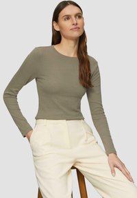 Olijfgroene lange mouwen top in ribbelstructuur, gecombineerd met crèmekleurige broek. De top heeft een ronde halslijn en een aansluitende silhouette.