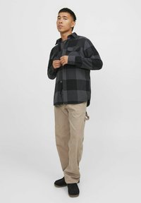 Zwart en grijs geruit flanellen overhemd met een geblokte patroon, twee borstzakken, knoopsluitingen en lange mouwen, gecombineerd met beige broek en zwarte schoenen.