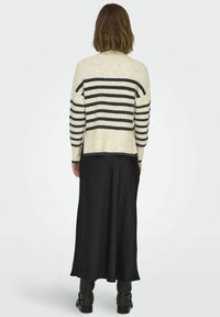 Le pull en tricot présente des rayures horizontales crème et noires, avec une coupe décontractée et un ourlet côtelé. Associé à une jupe noire longue et des bottes.