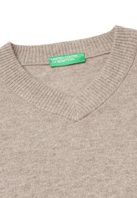 Beżowy sweter w serek, wykonany z prążkowanego materiału. Posiada teksturowane wykończenie oraz zieloną metkę z napisem "UNITED COLORS OF BENETTON."