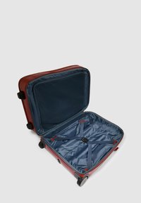 Rode harde koffer met een blauwe binnenkant, voorzien van een patroonvoering, verstelbare riemen en soepel rollende wielen. Ritsafsluiting.