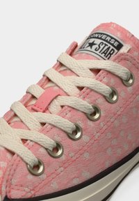 Ροζ αθλητικό παπούτσι Converse με λευκά πουά, λευκά κορδόνια, μεταλλικά ρουμπάκια και εμφανές λογότυπο All Star στη γλώσσα.