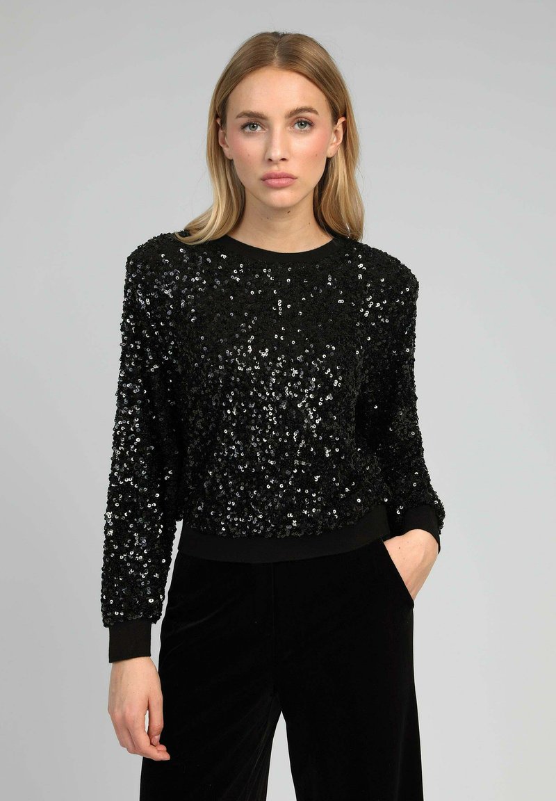 Sweatshirt noir à sequins avec un col rond, des manches longues et des poignets et un ourlet côtelés. La texture est brillante et réfléchissante, créant un design superposé.