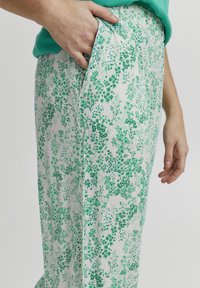 Pantalones estampados con flores en blanco y verde. Hechos de tejido ligero, con un corte relajado y bolsillos laterales, que exhiben un patrón inspirado en la naturaleza.