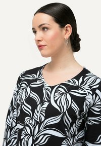 Černobílá blůza se květinovým vzorem, vyrobená z lehkého materiálu, s výstřihem do V a dlouhými rukávy.